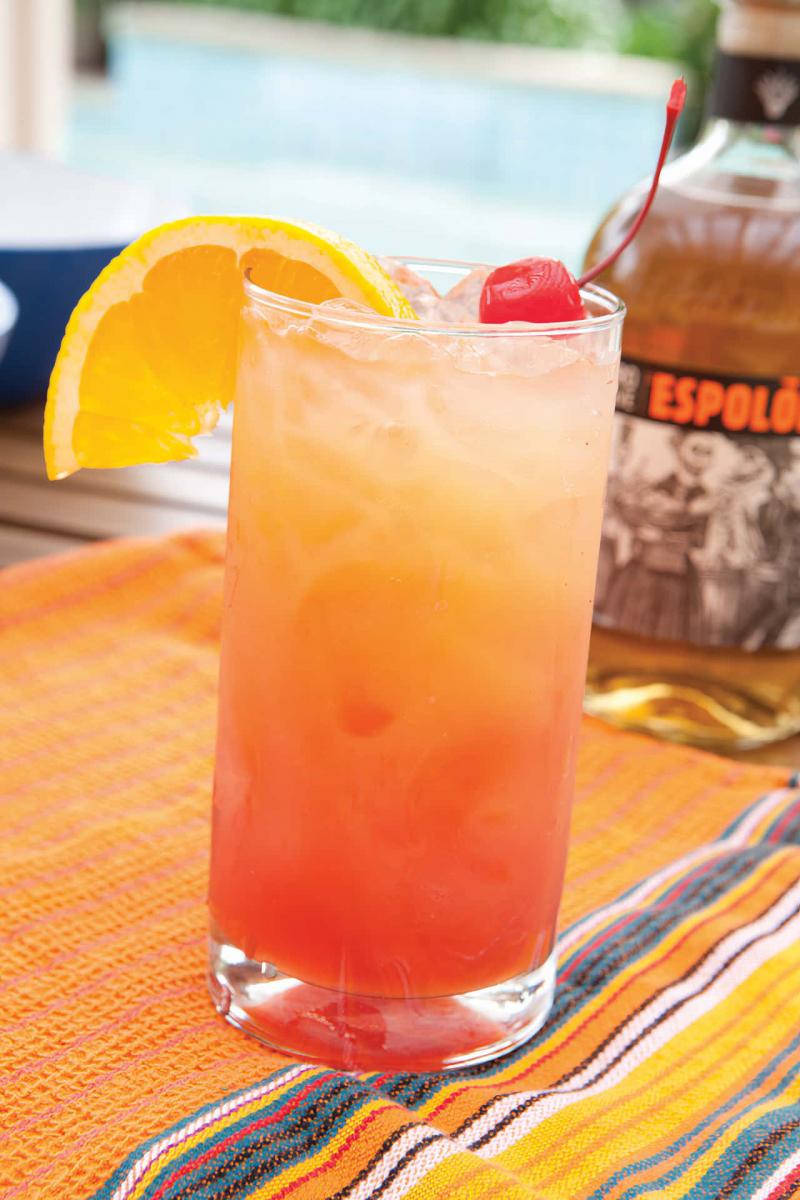 Tequila sunrise in a high ball glass on a beach blanket near a swimming pool